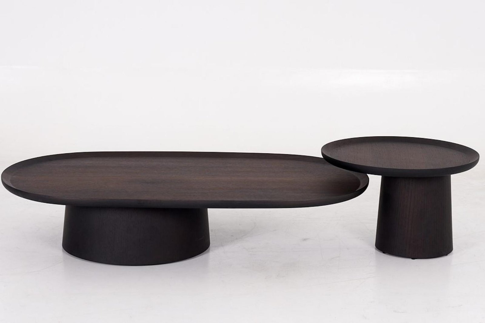 Low dark oval coffee table overlapping a smaller higher round table