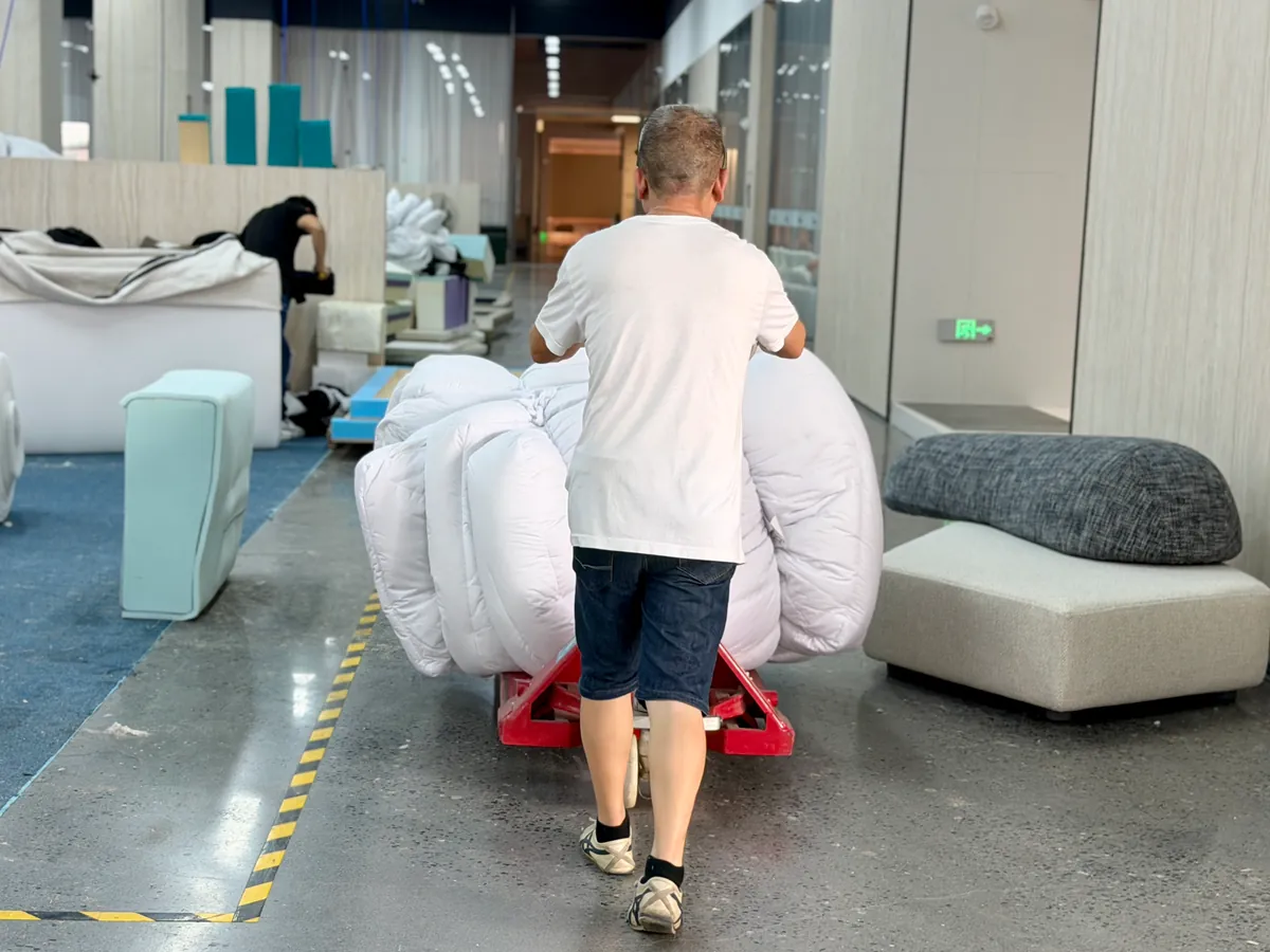 Worker moving a covered upholstered furniture piece on a wheeled trolley