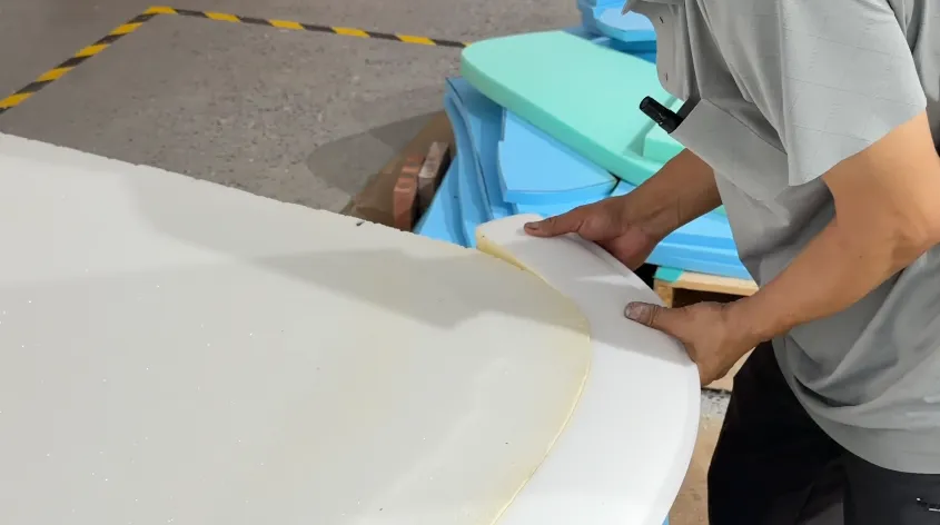 Worker shaping a white upholstery component beside foam pieces in a workshop