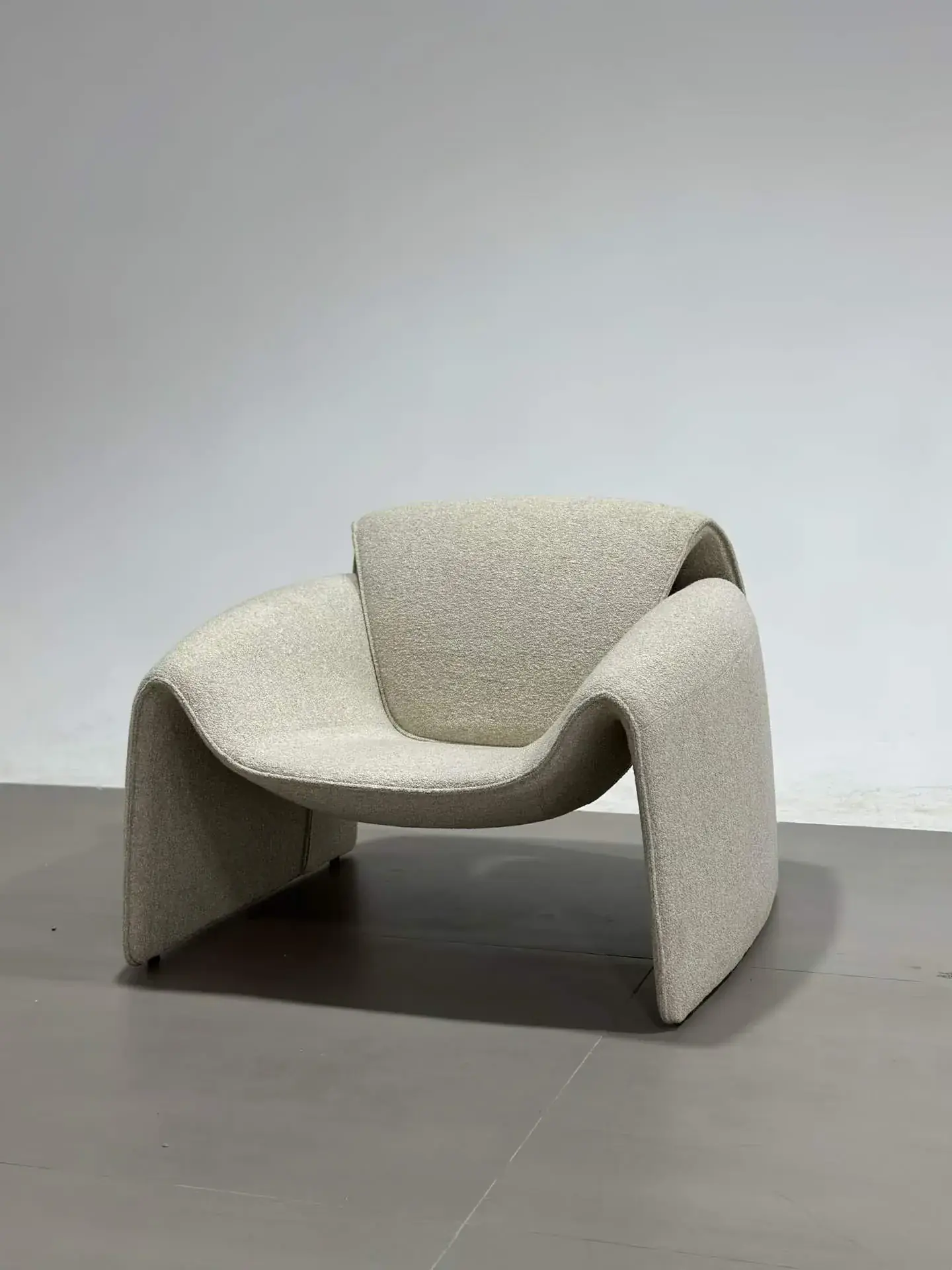 Light-colored sculptural upholstered chair with curved arms and a low seat