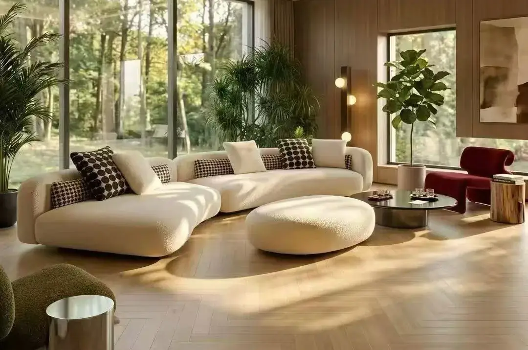 Light curved sofa and round upholstered ottoman arranged beside tall windows