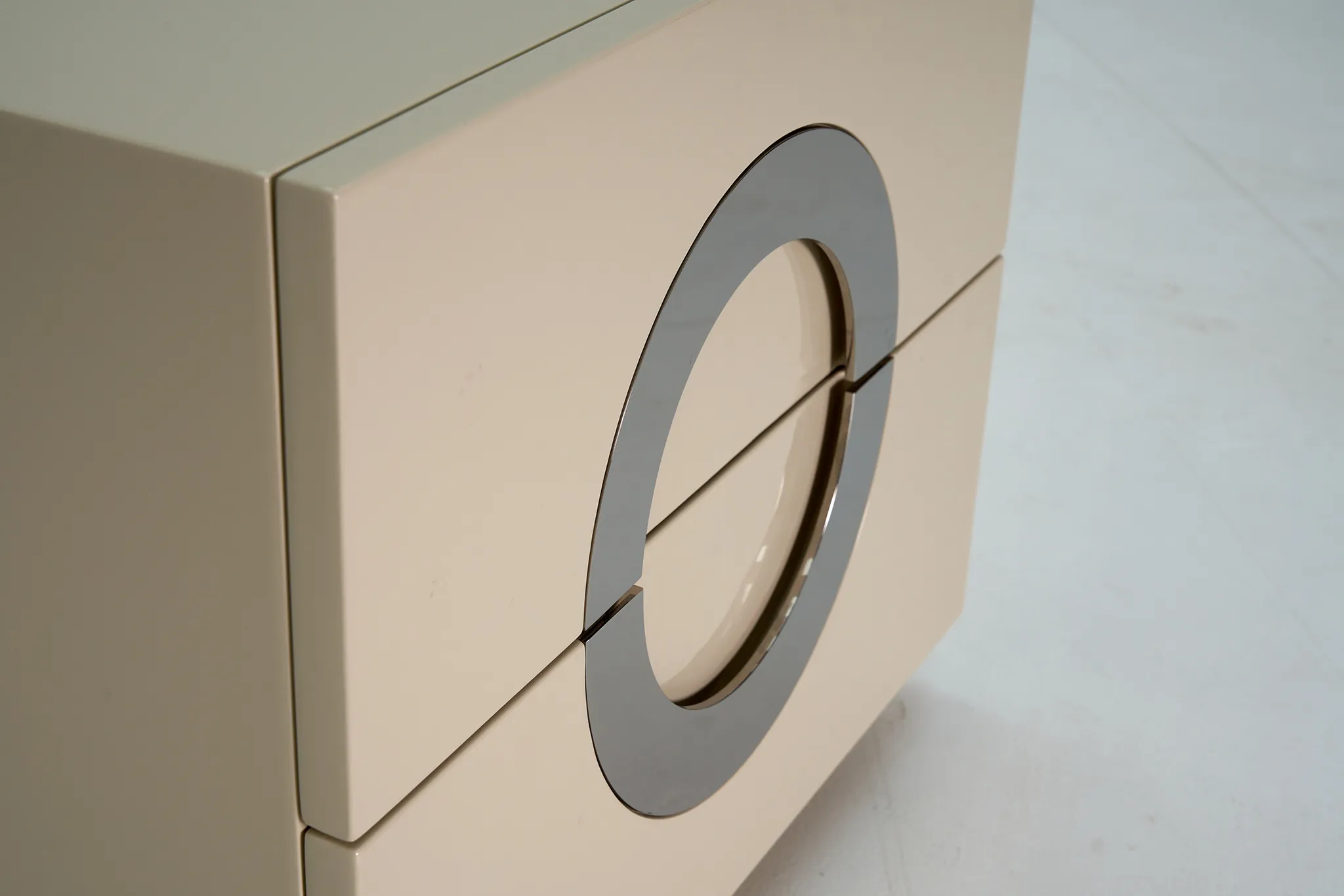 Close detail of a pale cabinet front with a circular decorative handle and reflective finish