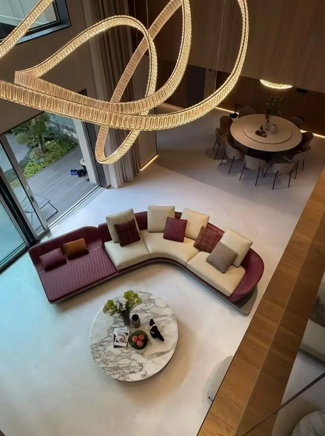 View down into a tall open living space with a curved sofa group and a dining table beyond