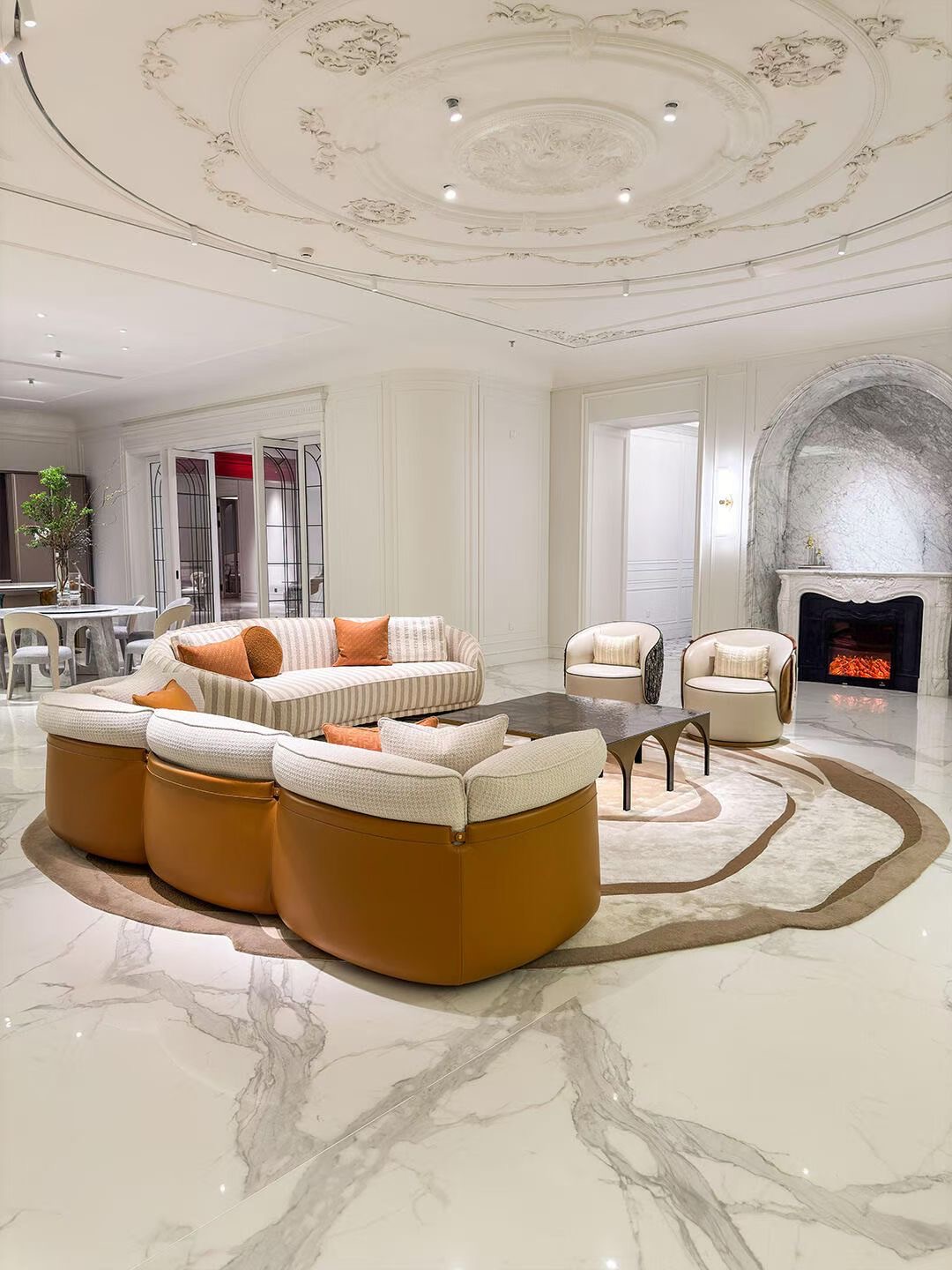 Large pale living room with curved upholstered seating, a round table and decorative ceiling