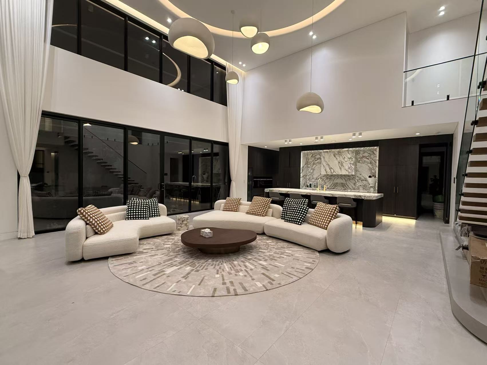 Double-height living room with low pale seating, a round rug and suspended ceiling lights