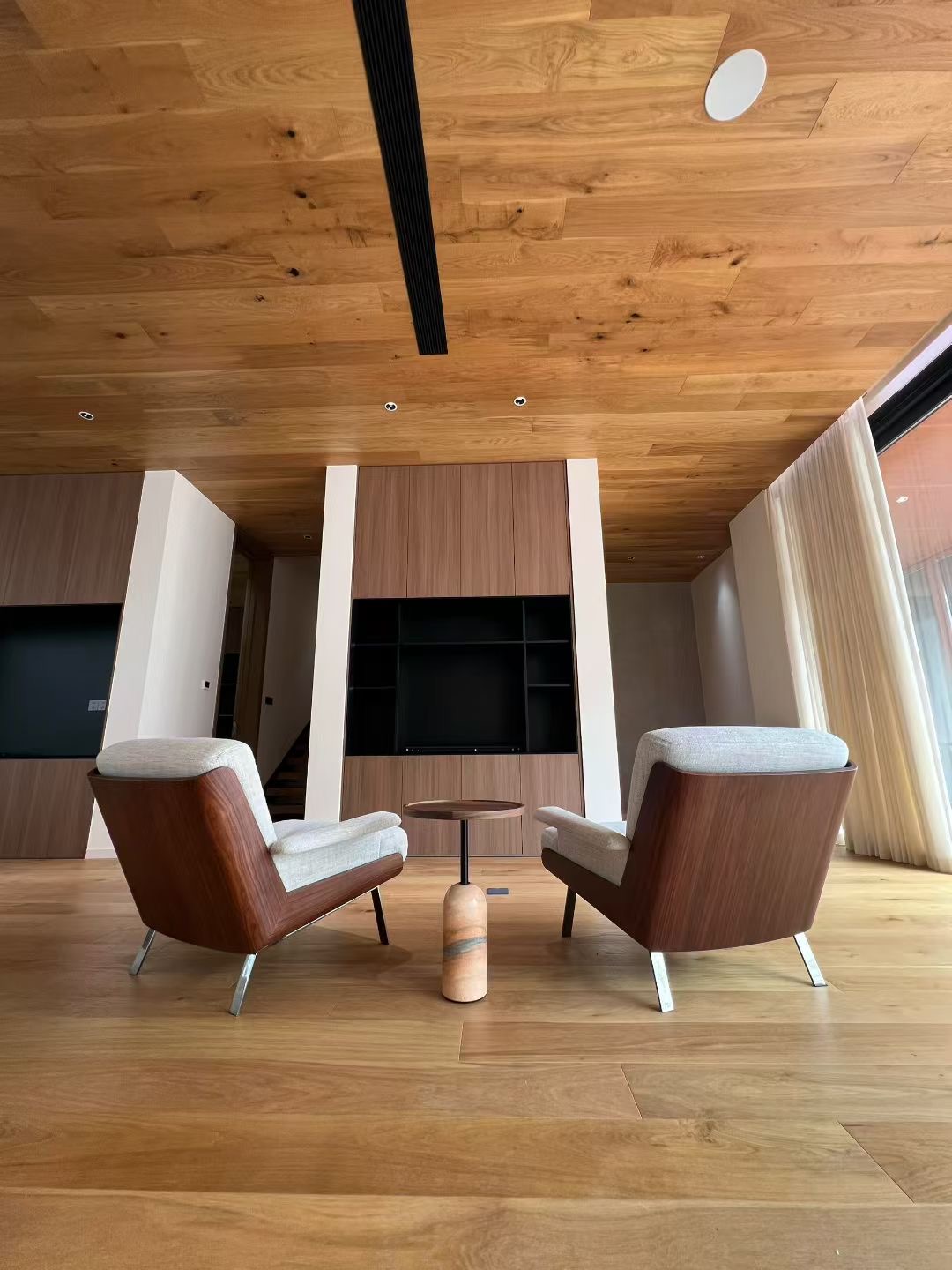 Two lounge chairs and a small table in a glazed corner with a wood-toned ceiling
