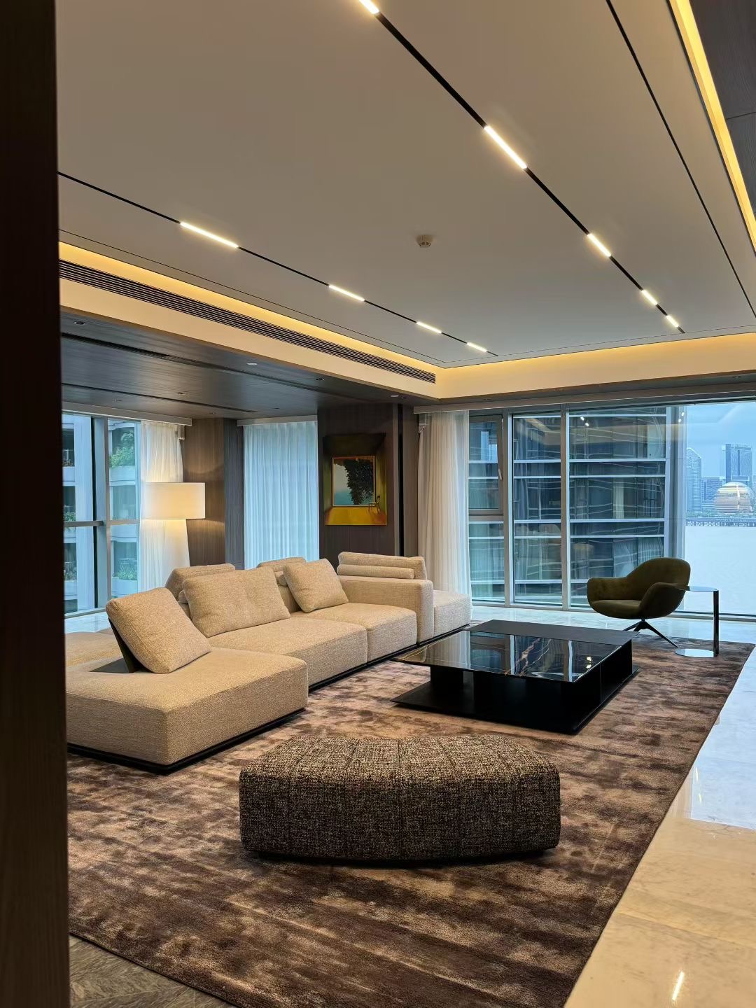 Sofa, lounge chair and ottoman grouped around a coffee table beside broad living-room windows
