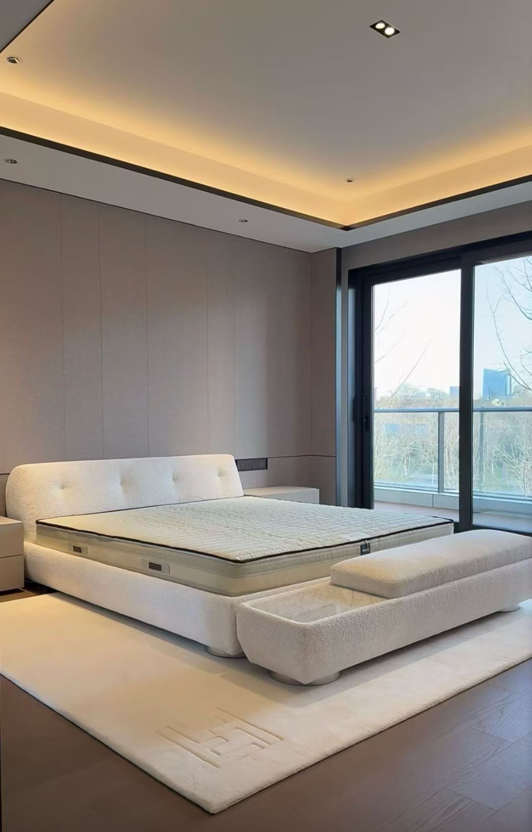 Low upholstered bed, foot-end bench and rug arranged beside a large bedroom window